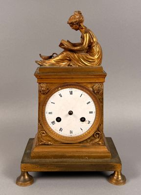 a gold clock with a woman sitting on top of it