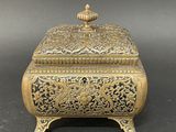 an ornate brass box with a lid on a black background