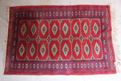 un vieux tapis rouge orné d'un motif en losanges, posé sur un sol blanc