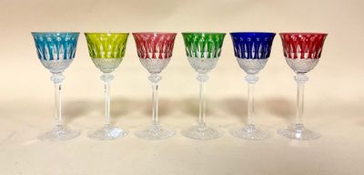 six verres à vin colorés alignés en rang sur une surface blanche