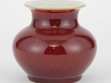 un vase rouge avec un couvercle blanc posé sur une table