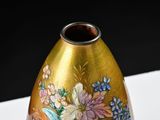 a gold vase with flowers painted on it sitting on a table