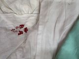 a white shirt with red flowers on it laying on a bed