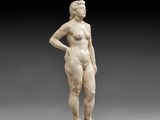 une statue représentant une femme debout, les mains sur les hanches
