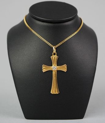 a gold cross necklace with a diamond on a black mannequin