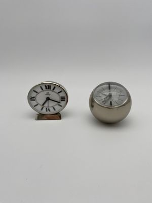une paire de petites horloges en argent posées l'une à côté de l'autre sur une surface blanche