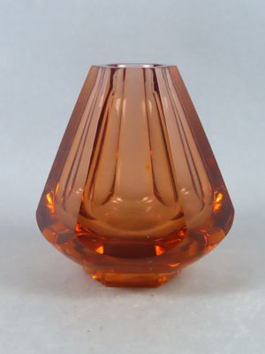 un petit vase en verre orange posé sur une surface blanche