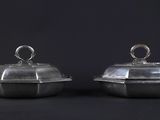 pair of silverplated dishes with domed lids on a black background