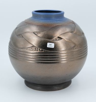 un vase argenté avec un couvercle bleu posé sur une surface blanche
