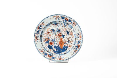 assiette bleue et blanche ornée de fleurs orange sur un socle, sur fond blanc