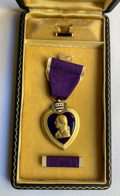 une médaille violette en forme de cœur, dans un écrin doré, entourée d'un ruban violet