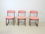 three pink chairs sitting next to each other against a white wall
