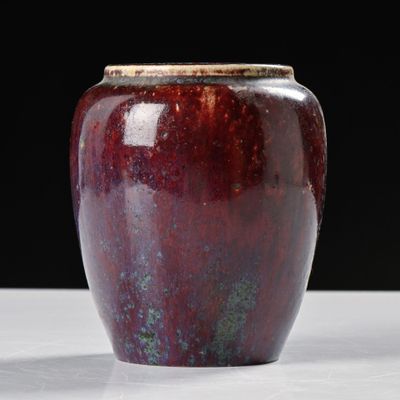 un vase rouge posé sur une table, sur fond noir
