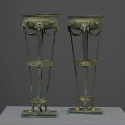 pair of bronze vases on a white pedestal against a gray background