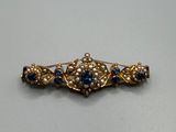 un gros plan d'une broche en or sertie de pierres bleues et blanches