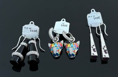 trois paires de boucles d'oreilles et une paire de ciseaux posés sur une surface noire