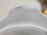 a close up of a white vase with a flower in the background