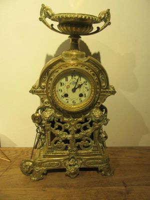 a gold clock sitting on a wooden table with a vase on top