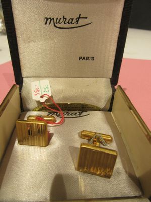 pair of gold cufflinks in a box on a pink surface