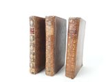 three old books are stacked on top of each other on a white surface