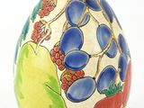 un œuf peint, orné de fruits, posé sur un fond blanc