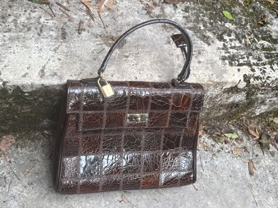 un sac à main marron posé par terre près d'un mur de pierre