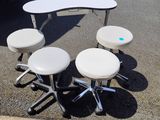 plusieurs tabourets et une table dans un parking, avec une camionnette en arrière-plan