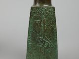a green vase with a bird on it sitting on a table