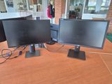 three computer monitors on a table with a woman standing in the background