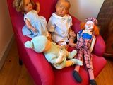 trois poupées assises sur une chaise rouge dans une pièce