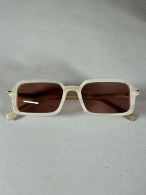 lunettes de soleil beiges aux verres marron, posées sur une surface blanche