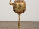 a gold tea pot on a stand on a wooden floor