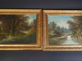 two framed paintings of a river and trees on a table