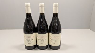 trois bouteilles de vin rouge sont posées sur une table devant un mur blanc