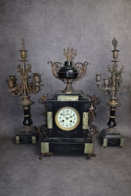 une horloge noire posée sur une table, à côté d'un bouquet de bougies