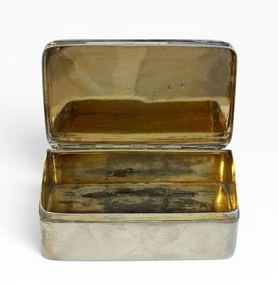 une petite boîte argentée avec un couvercle, posée sur une surface blanche