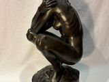 bronze statue of a man sitting on a rock with his hands on his knees