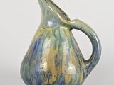 un vase bleu et vert muni d'une anse, posé sur une surface blanche