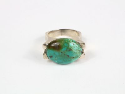 un gros plan d'une bague sertie d'une pierre turquoise sur une surface blanche