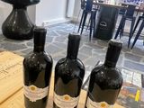 three bottles of wine sitting on top of a wooden table next to a cutting board