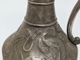 a silver vase with a bird on it on a white surface
