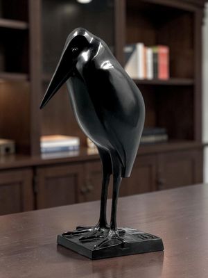 une statue représentant un oiseau noir, posée sur une table devant une bibliothèque