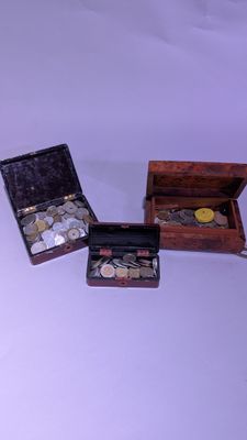 trois petites boîtes en bois contenant des pièces de monnaie, posées sur une surface blanche