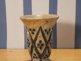 un petit vase posé sur une table, avec un mur rayé en arrière-plan