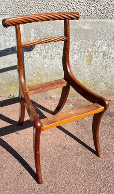 a wooden chair sitting on a sidewalk next to a cement wall