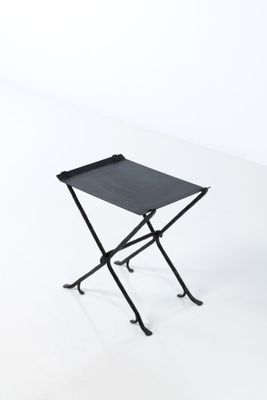 le petit tabouret pliant noir est posé sur une surface blanche