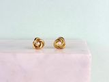 a pair of gold earrings on top of a marble block