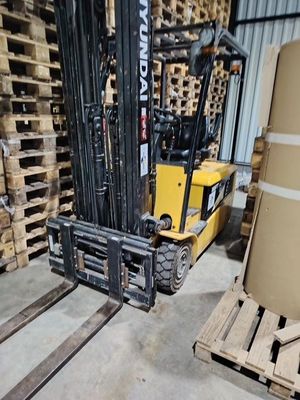 un chariot élévateur dans un entrepôt, avec des palettes de bois en arrière-plan