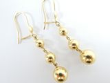 boucles d'oreilles pendantes en forme de boules dorées sur fond blanc