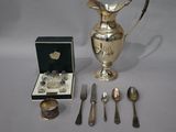 a silver pitcher, spoons, and other silverware on a table